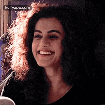 A Woman With Curly Hair Is Smiling And Wearing A Black Top . GIF