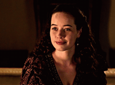 A Woman With Curly Hair Is Smiling And Wearing A Purple Dress GIF