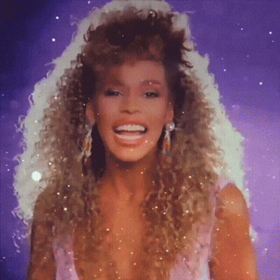 A Woman With Curly Hair Is Smiling And Wearing Earrings GIF