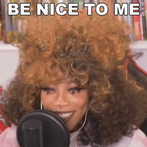 A Woman With Curly Hair Is Smiling In Front Of A Microphone And Saying Be Nice To Me GIF