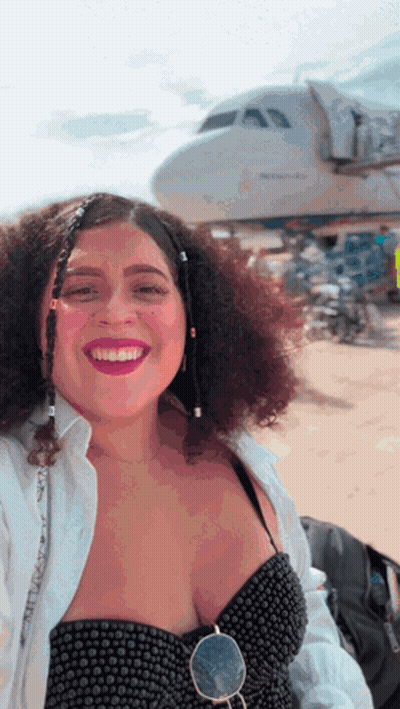 A Woman With Curly Hair Is Smiling In Front Of A Plane That Says United Airlines GIF