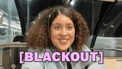 A Woman With Curly Hair Is Smiling In Front Of A Sign That Says " Blackout " GIF