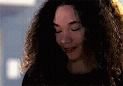 A Woman With Curly Hair Is Smiling With Her Eyes Closed And Looking Down . GIF