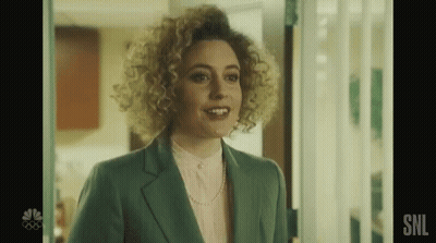 A Woman With Curly Hair Is Standing In A Doorway Wearing A Green Suit And A Pink Shirt . GIF