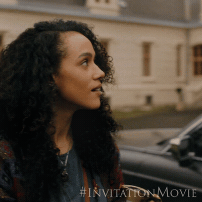 A Woman With Curly Hair Is Standing In Front Of A Car With # Invitationmovie Written On The Bottom GIF