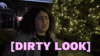 A Woman With Curly Hair Is Standing In Front Of A Christmas Tree And Says [ Dirty Look ] GIF