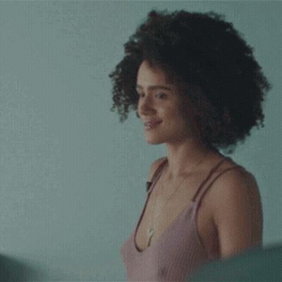 A Woman With Curly Hair Is Standing In Front Of A Mirror And Smiling . GIF