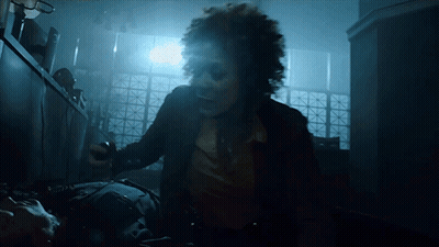 A Woman With Curly Hair Is Standing In Front Of A Window GIF
