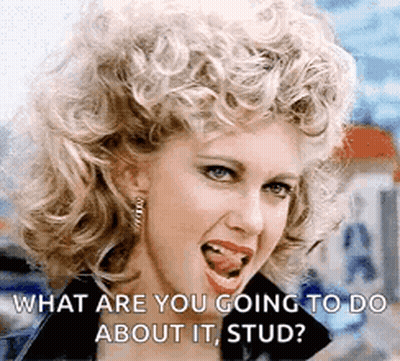 A Woman With Curly Hair Is Sticking Her Tongue Out And Asking What Are You Going To Do About It , Stud . GIF