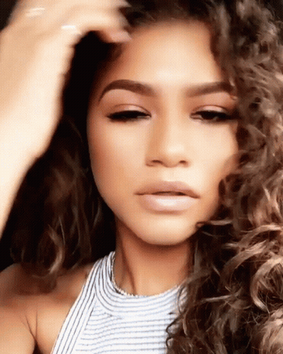 A Woman With Curly Hair Is Taking A Selfie With Her Hand In Her Hair . GIF