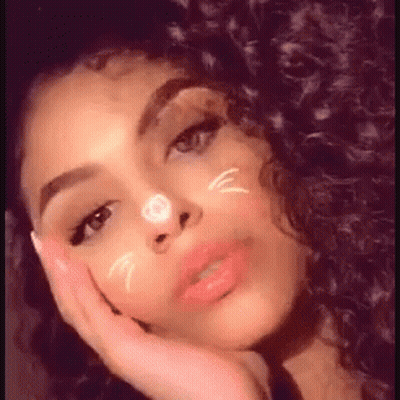 A Woman With Curly Hair Is Taking A Selfie With Her Hand On Her Face And A Cat Face On Her Face . GIF