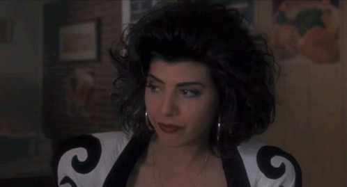 A Woman With Curly Hair Is Wearing A Black And White Jacket With The Letter G On It . GIF