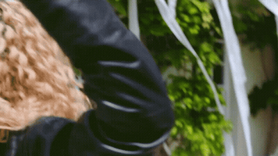 A Woman With Curly Hair Is Wearing A Black Jacket GIF
