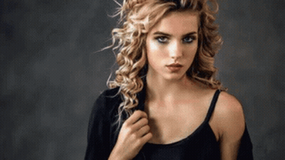A Woman With Curly Hair Is Wearing A Black Tank Top And A Jacket . GIF