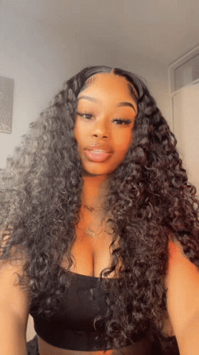 A Woman With Curly Hair Is Wearing A Black Top And A Necklace GIF