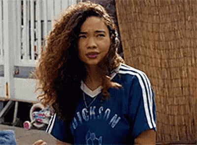 A Woman With Curly Hair Is Wearing A Blue Shirt With White Stripes And A Necklace . GIF