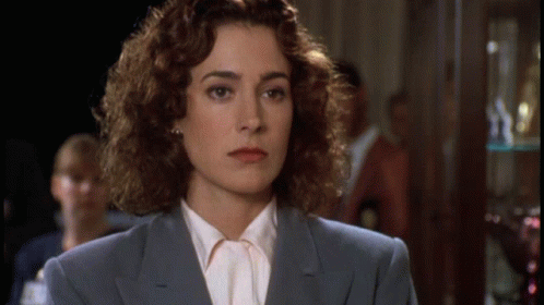 A Woman With Curly Hair Is Wearing A Blue Suit And A White Shirt GIF