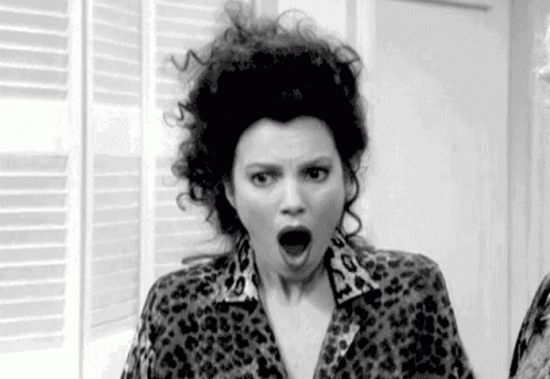 A Woman With Curly Hair Is Wearing A Leopard Print Shirt And Making A Surprised Face . GIF