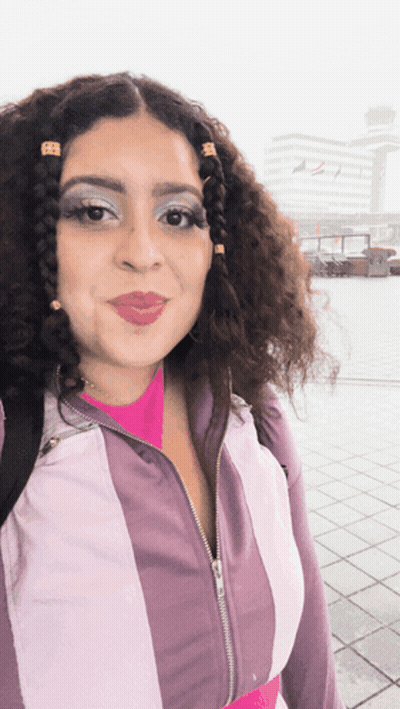 A Woman With Curly Hair Is Wearing A Purple And White Striped Jacket GIF