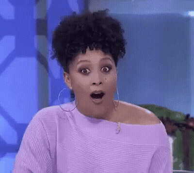 A Woman With Curly Hair Is Wearing A Purple Sweater And Hoop Earrings . GIF