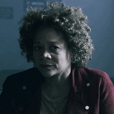 A Woman With Curly Hair Is Wearing A Red Jacket And Earrings GIF