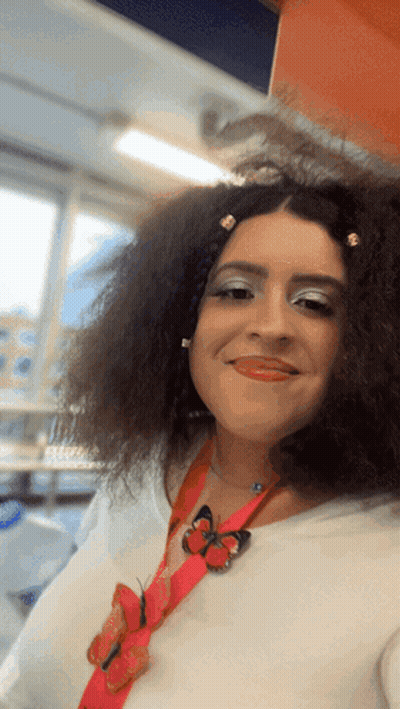 A Woman With Curly Hair Is Wearing A Red Lanyard With Butterflies On It GIF