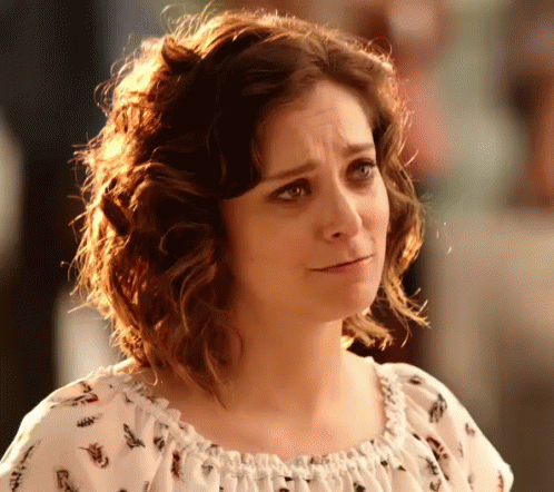 A Woman With Curly Hair Is Wearing A White Top With A Floral Print GIF