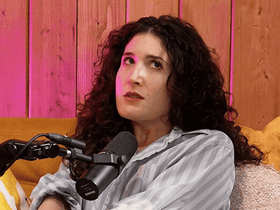 A Woman With Curly Hair Sitting In Front Of A Shure Microphone GIF