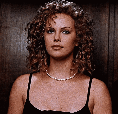 A Woman With Curly Hair Wearing A Black Tank Top And A Pearl Necklace GIF