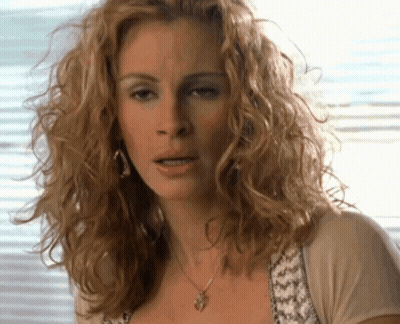 A Woman With Curly Hair Wearing A Necklace GIF
