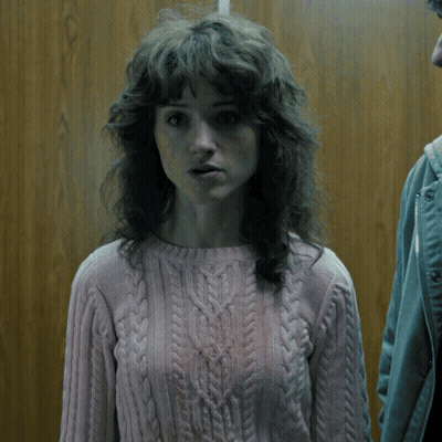 A Woman With Curly Hair Wearing A Pink Sweater Looks Surprised GIF