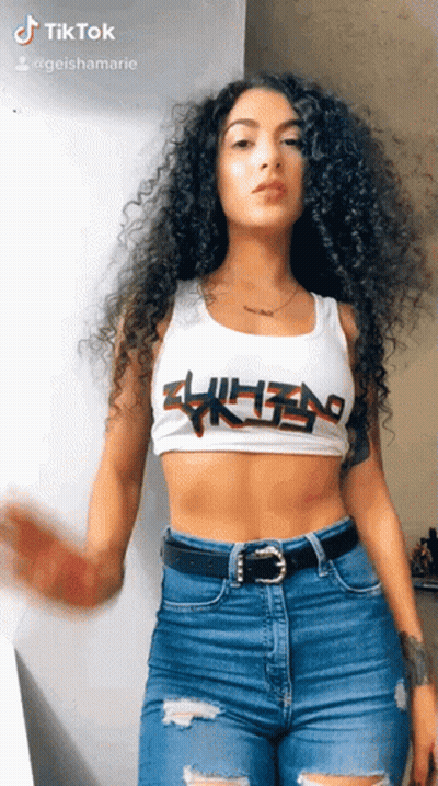 A Woman With Curly Hair Wearing A White Crop Top And Blue Jeans . GIF