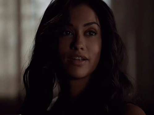 A Woman With Dark Hair Is Smiling In The Dark GIF