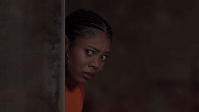 A Woman With Dreadlocks And Hoop Earrings Is Leaning Against A Wall GIF