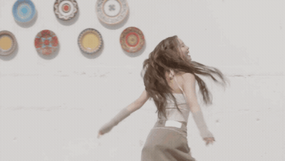 A Woman With Dreadlocks Is Dancing In Front Of Plates On A Wall GIF