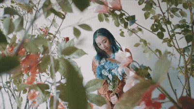 A Woman With Dreadlocks Is Holding A Bouquet Of Flowers GIF