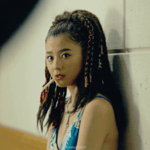 A Woman With Dreadlocks Is Leaning Against A Wall And Smoking GIF