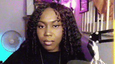 A Woman With Dreadlocks Is Sitting In Front Of A Microphone In A Room With A Fan . GIF