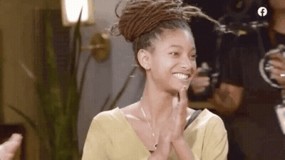 A Woman With Dreadlocks Is Smiling And Clapping Her Hands While Wearing A Yellow Shirt . GIF