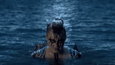 A Woman With Face Paint Is Swimming In The Water At Night GIF