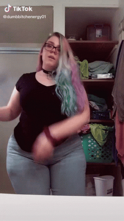 A Woman With Glasses And A Choker Is Dancing In Front Of A Mirror In A Bathroom . GIF