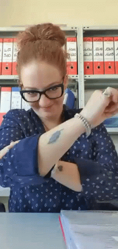 A Woman With Glasses And A Tattoo On Her Arm Is Sitting At A Table . GIF