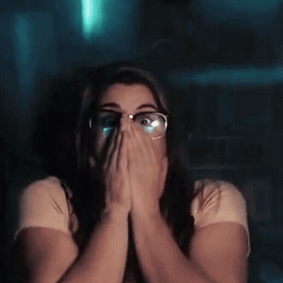 A Woman With Glasses Is Covering Her Face With Her Hands While Watching A Movie . GIF