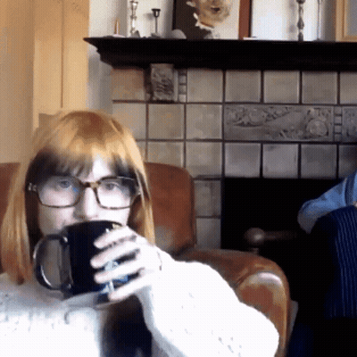 A Woman With Glasses Is Drinking From A Black Mug GIF