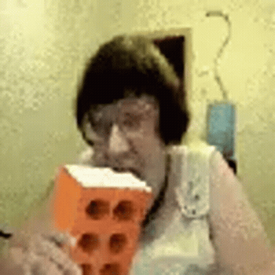 A Woman With Glasses Is Eating A Brick . GIF