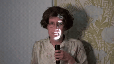 A Woman With Glasses Is Holding A Flashlight With A Face Projected On It GIF