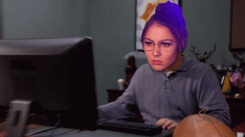 A Woman With Glasses Is Sitting In Front Of A Computer Screen GIF