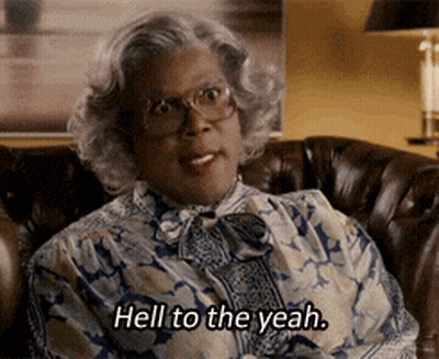 A Woman With Glasses Is Sitting On A Couch And Says Hell To The Yeah . GIF
