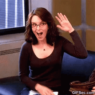 A Woman With Glasses Is Sitting On A Couch And Waving Her Hand . GIF