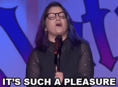 A Woman With Glasses Is Standing In Front Of A Microphone And Saying It 'S Such A Pleasure . GIF